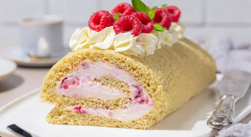 Himbeer Biskuitrolle mit Sahne und frischen Beeren, ein Genuss für jeden Kaffeetisch.