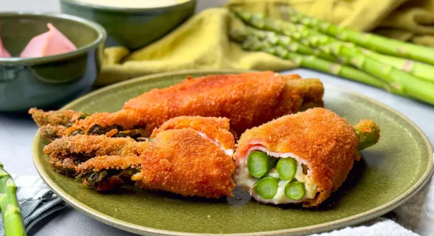 Knusprig paniertes Spargel Cordon Bleu mit Schinken und Käse gefüllt, auf einem grünen Teller angerichtet.