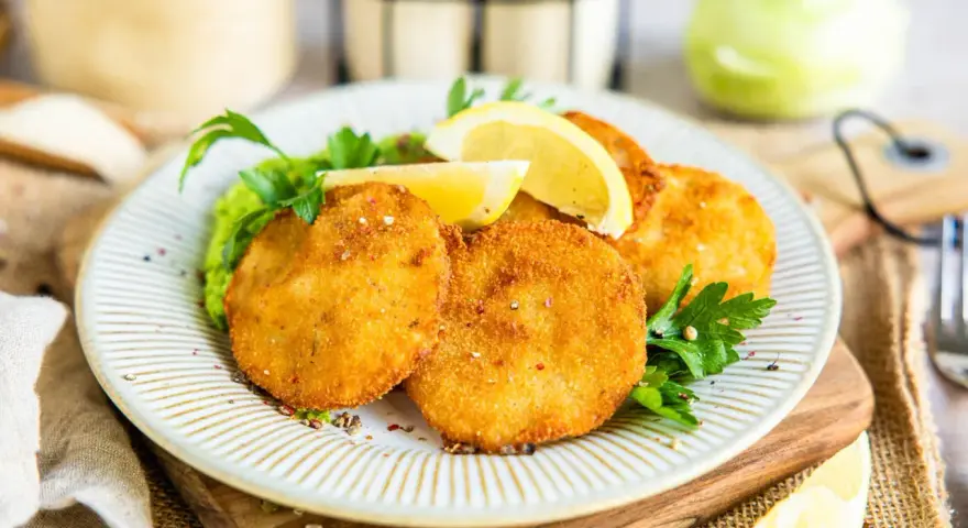 Knuspriges Kohlrabi Schnitzel auf einem Teller mit Erbsenpüree, Zitrone und Petersilie. Ein Genuss für Vegetarier!