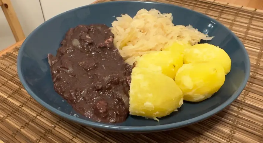 Ein Teller mit deftigem Essen: dunkle Soße, Sauerkraut und Salzkartoffeln. Erinnert an die gute, alte tote Oma.