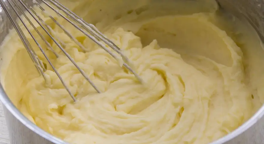 Cremiger kartoffelbrei ohne butter wird mit einem Schneebesen in einem Topf zubereitet.
