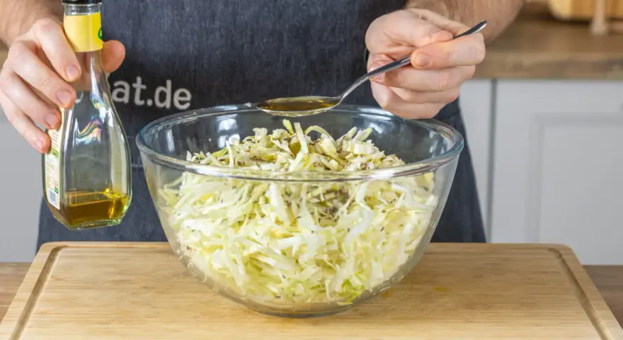 Ein Löffel Öl wird über den fein geschnittenen Spitzkohl gegeben, der für Omas Spitzkohlsalat vorbereitet wird.