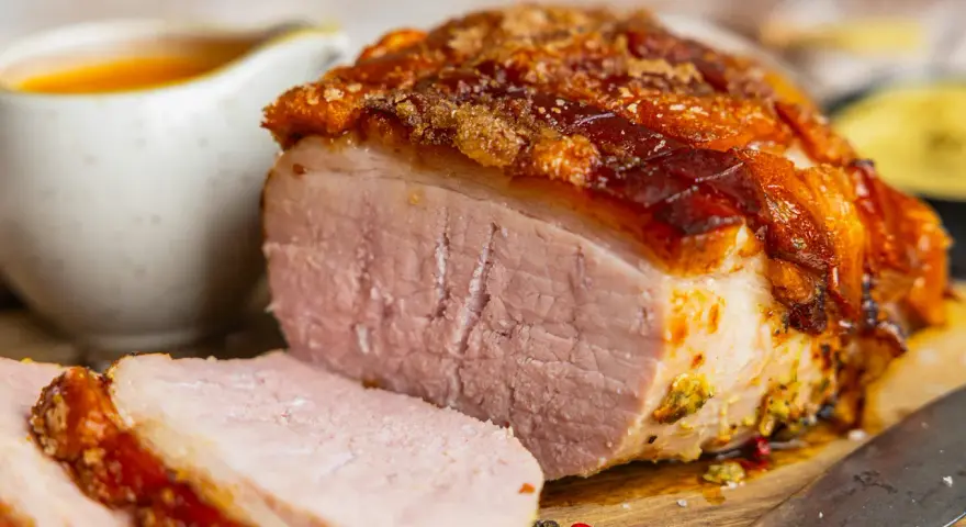 Saftiger Braten mit knuspriger Kruste, perfekt für die Zubereitung von Prager Schinken im Backofen. Dazu eine Schüssel mit Sauce.