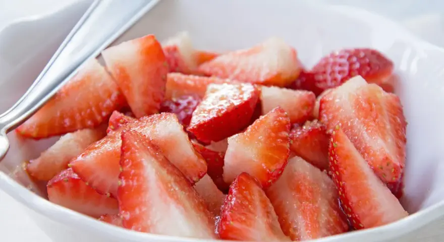 Schüssel mit marinierten Erdbeeren, die mit einem Löffel serviert werden. Saftige, rote Erdbeerstücke glänzen im Licht.