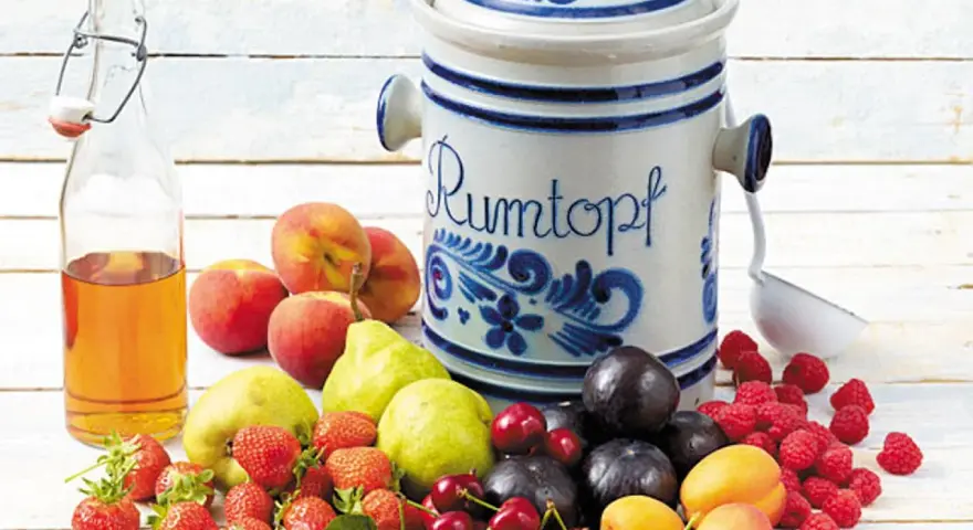 Früchte für ein Rumtopf Rezept nach Oma: Erdbeeren, Kirschen, Aprikosen, Pflaumen, Pfirsiche, Birnen, Himbeeren und eine Flasche Schnaps.