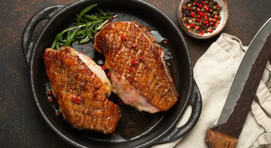 Zwei perfekt gebratene Entenbrüste in einer Pfanne, garniert mit Rosmarin und rosa Pfeffer. Ein klassisches Entenbrust Rezept, bereit zum Servieren.