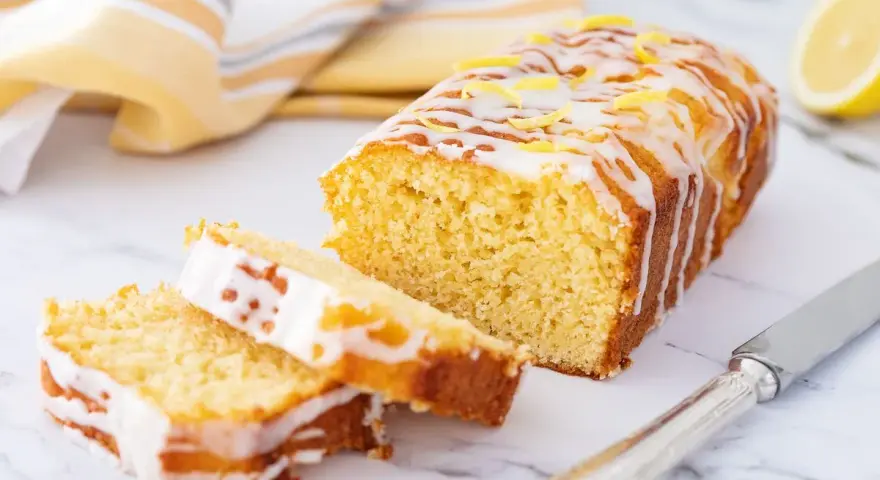 Saftiger zitronenkuchen mit Joghurt, überzogen mit Zuckerguss und garniert mit Zitronenschale. Ein Stück ist angeschnitten.