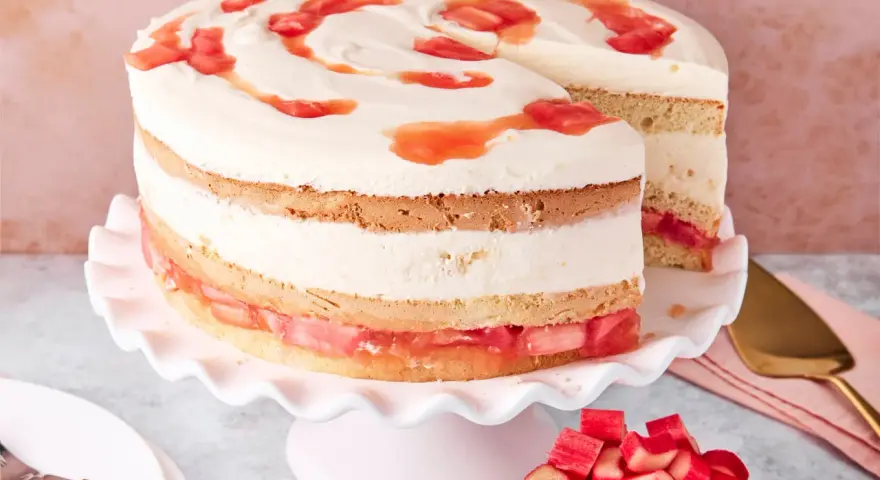 Eine köstliche Erdbeer Rhabarber Torte mit Sahne und Fruchtstücken, auf einem rosa Tortenständer präsentiert.
