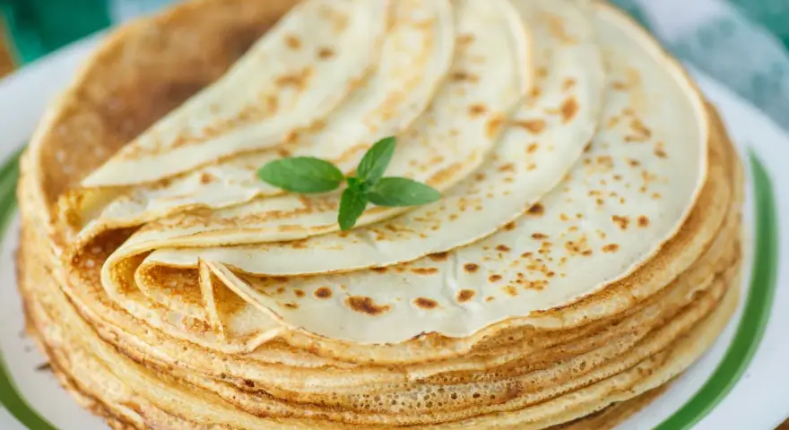 Ein Stapel goldbrauner Pfannkuchen, wie nach Omas Pfannkuchen Rezept gemacht, mit einem Minzblatt garniert.