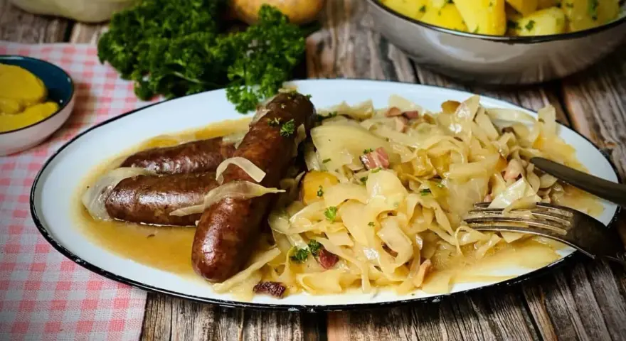 Deftige Bratwürste mit Zwiebeln auf bayrisch Kraut, garniert mit Petersilie. Dazu Salzkartoffeln und Senf.