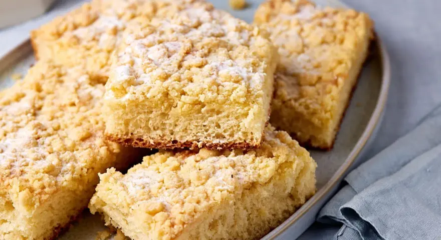 Saftiger Streuselkuchen vom Blech, mit Puderzucker bestäubt, liegt auf einem Teller.