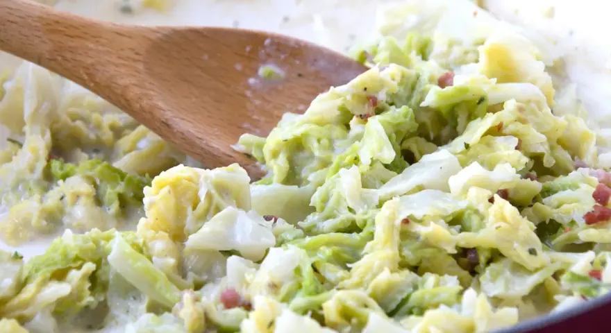 Cremiger Wirsing mit Speck, zubereitet mit einem Holzlöffel. Ein leckeres Gericht, das Lust auf mehr wirsing rezepte macht.