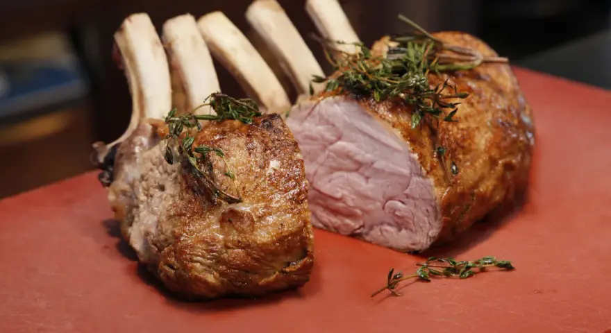 Ein gebratener Semerrolle Kalb mit Kräutern auf rotem Untergrund.