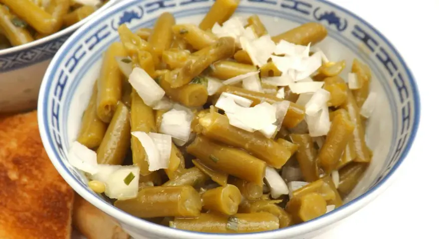Bohnensalat rezept: Grüne Bohnen mit Zwiebeln in einer Schüssel, daneben geröstetes Brot.