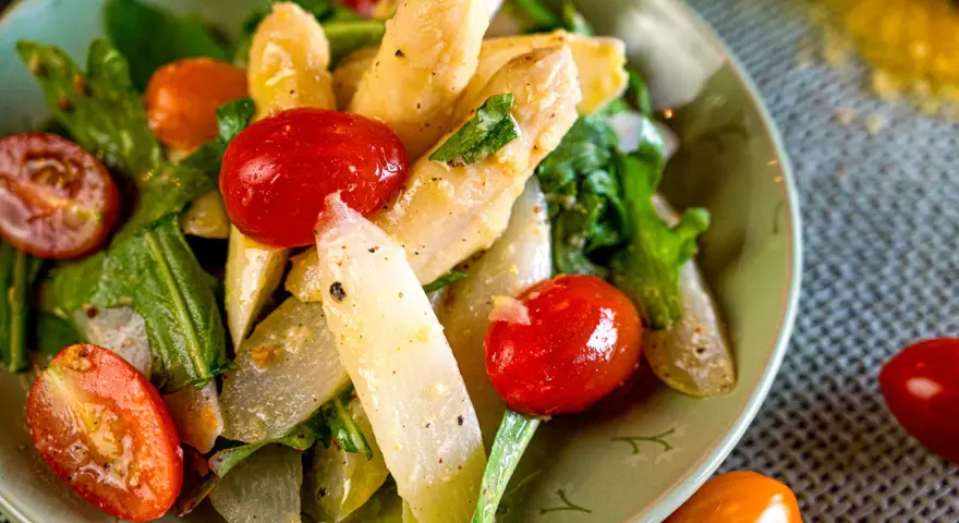 Ein Teller mit weltbestem Spargelsalat, garniert mit Kirschtomaten und frischen Kräutern. Ein Genuss für Augen und Gaumen.