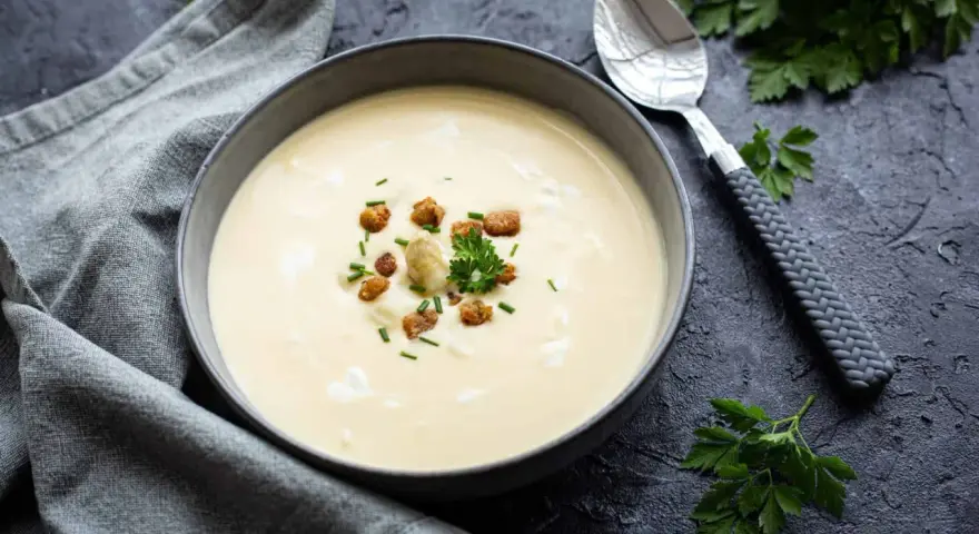 Cremige Spargelsuppe aus Schalen, garniert mit Croutons und frischen Kräutern. Ein Löffel liegt daneben.