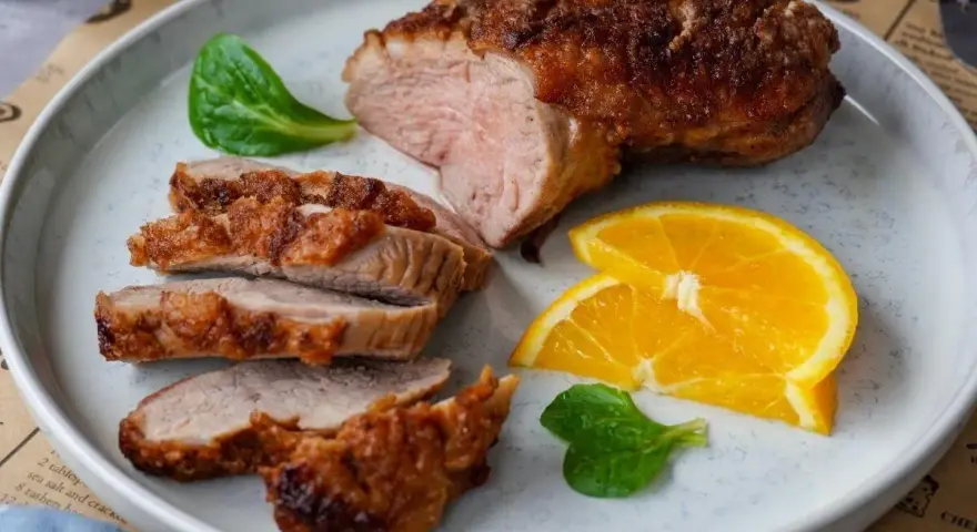 Saftige entenbrust im airfryer, perfekt gebräunt und in Scheiben geschnitten, serviert mit frischen Orangenscheiben und grünen Blättern.