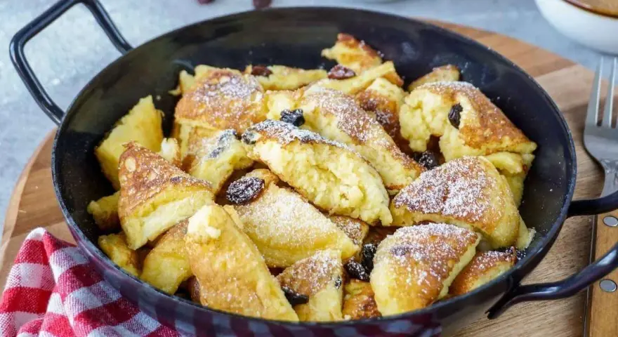Leckerer, schneller Kaiserschmarrn im Backofen, bestäubt mit Puderzucker und Rosinen, serviert in einer Pfanne.