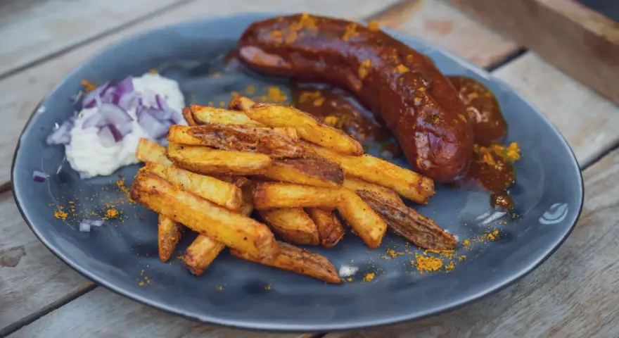 Eine saftige Currywurst im Backofen mit knusprigen Pommes und einem Klecks Mayo mit Zwiebeln.