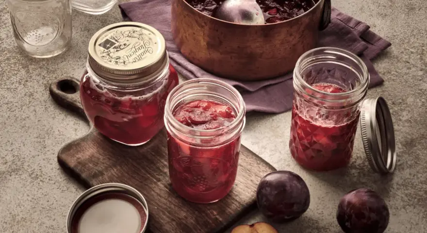 Frisch eingekochte Pflaumenmarmelade im Glas, bereit für das pflaumenmarmelade rezept. Frische Pflaumen liegen daneben.