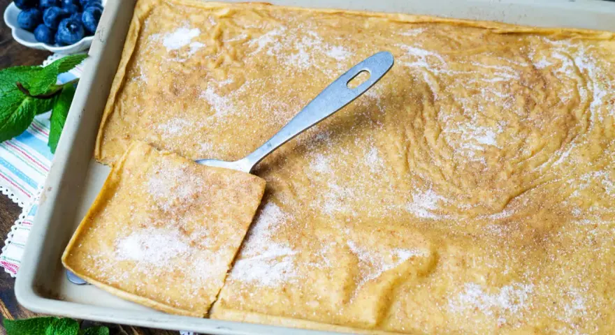 Großer, goldbrauner Ofenpfannkuchen mit Zucker und Zimt bestreut, bereit zum Servieren. Blaubeeren und Minze garnieren.