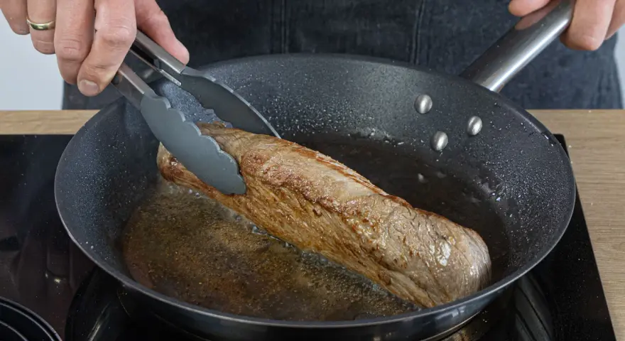 Ein saftiges Schweinefilet brät in der Pfanne. Einfache Rezepte für zartes Fleisch in der Pfanne gelingen so.