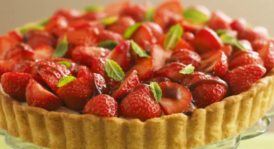 Ein köstlicher Erdbeerkuchen ohne Pudding, üppig belegt mit frischen Erdbeeren und Minze, auf einem Tortenständer.