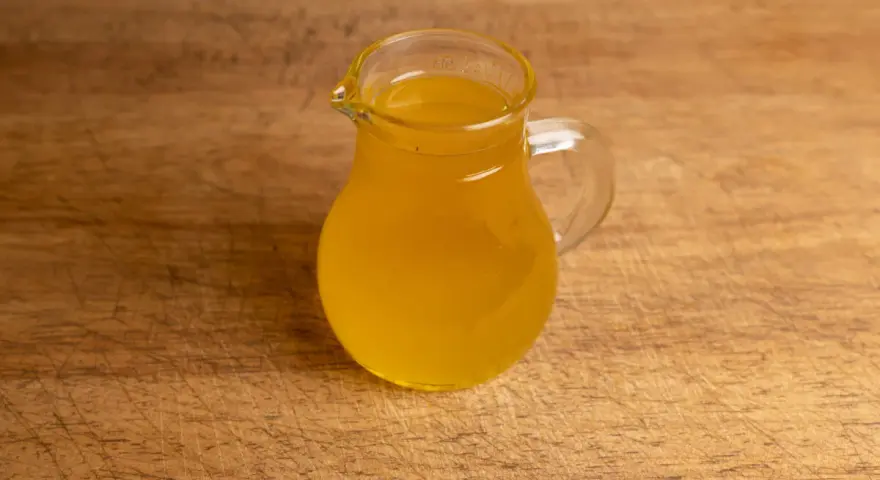Ein kleines Glas mit goldgelbem Butterschmalz steht auf einem Holzbrett. Perfekt zum butterschmalz selber machen.