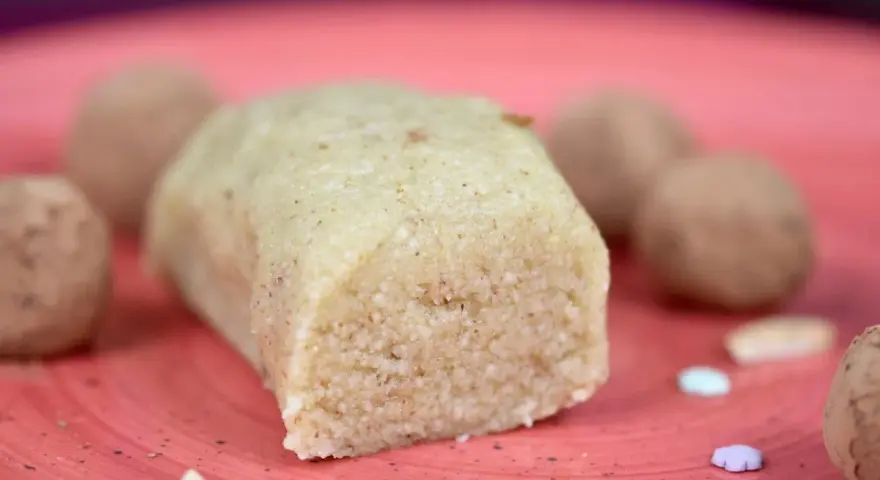 Ein Block selbstgemachtes Marzipan, ohne Rosenwasser, liegt auf einer roten Platte. Daneben sind Pralinen und bunte Zuckerstreusel.