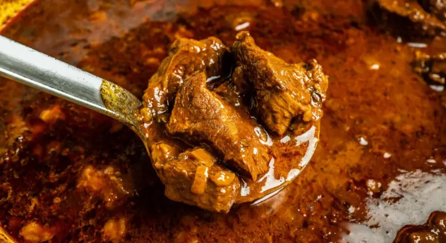 Ein Löffel voller herzhaftem Wildschweingulasch, bereit zum Servieren. Dieses Wildschweingulasch Rezept verspricht ein köstliches Gericht.