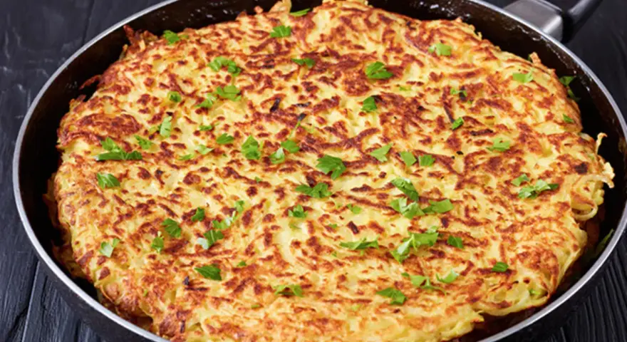 Goldbraune Kartoffel-Rösti in einer Pfanne, garniert mit Petersilie. Ein einfaches und leckeres schales Rezept für jeden Tag.
