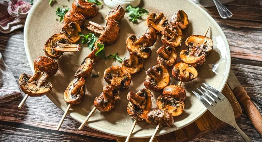 Gegrillte Champignons am Spieß, mit Kräutern verfeinert, auf einem Teller serviert. Ein Genuss für jeden Pilzliebhaber!