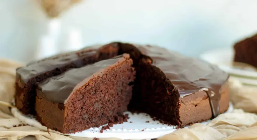 Ein saftiger Schokokuchen mit glänzender Glasur, perfekt für jedes schokokuchen rezept. Ein Stück ist bereits angeschnitten.
