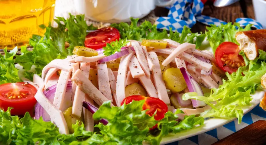 Ein leckerer Wurstsalat mit Gurken, Tomaten und Zwiebeln, garniert mit Salat. Perfekt für ein deftiges wurstsalat rezept.