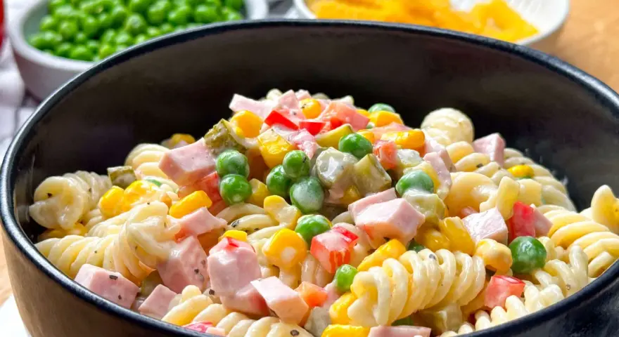 Ein cremiger nudelsalat mit mayonaise, garniert mit Erbsen, Mais, Paprika und Schinkenwürfeln.