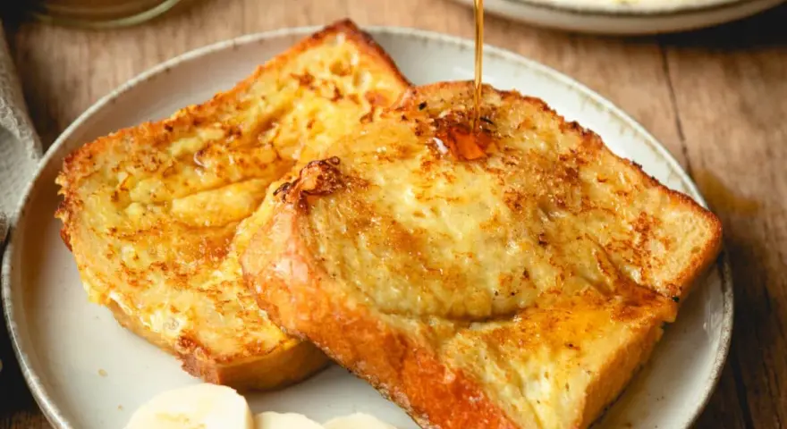 Armer Ritter, goldbraun gebraten, mit Sirup übergossen und Bananenscheiben garniert. Ein köstliches Frühstück!
