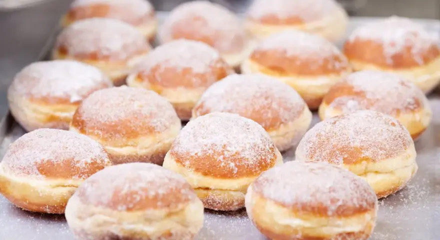 Eine Reihe von frisch gebackenen, mit Puderzucker bestäubten Berliner Pfannkuchen liegt auf einem Blech.