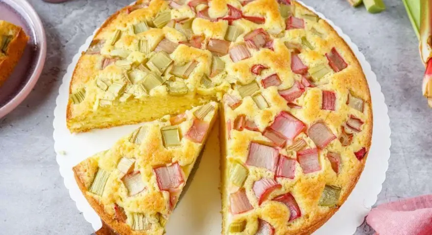 Saftiger Rhabarberkuchen, ein Klassiker unter den Rezepten mit Rhabarber. Ein Stück wird gerade herausgehoben.