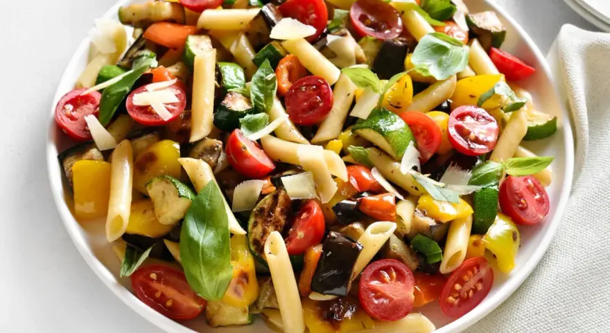 Bunter Nudelsalat ohne Mayo mit Penne, gegrilltem Gemüse, Kirschtomaten und Basilikum, garniert mit Parmesan.