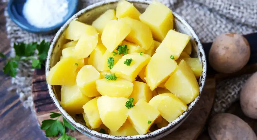 Schüssel mit dampfenden Salzkartoffeln, garniert mit Petersilie. Daneben eine kleine Schale mit Salz und rohe Kartoffeln.