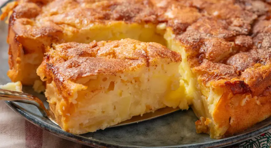 Ein Stück von einem goldbraunen, sehr feinen Apfelkuchen mit Zimt bestreut, wird mit einer Tortenheber herausgehoben.