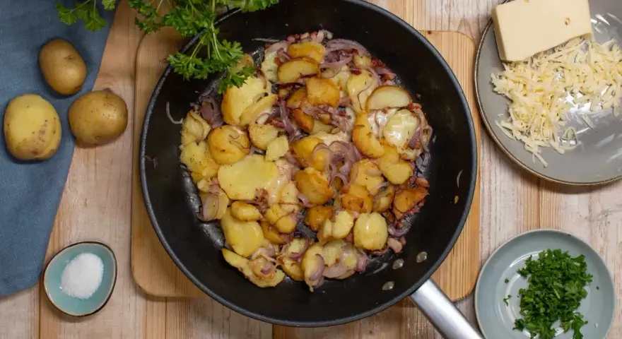 Bratkartoffeln mit Zwiebeln und Käse in der Pfanne, dazu frische Petersilie und Salz.