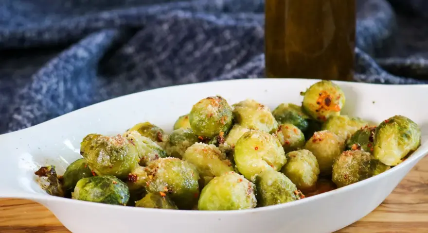 Ein weißes Ovalschälchen gefüllt mit knusprigem Rosenkohl, bestreut mit Parmesan und Chili-Flocken.
