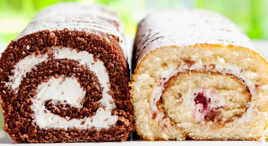 Zwei Biskuitrollen, eine schokoladig, die andere hell, mit Sahne und Fruchtfüllung, bestäubt mit Puderzucker. Wie von Landfrauen gebacken.
