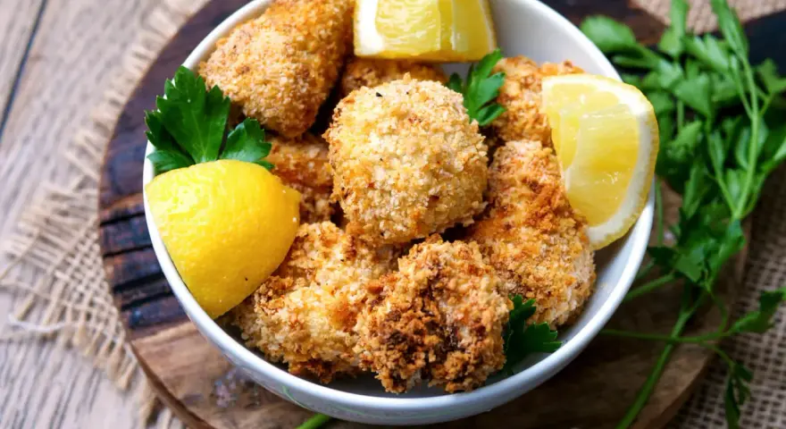 Knuspriger blumenkohl im airfryer, goldbraun paniert, serviert mit frischen Zitronenspalten und Petersilie.