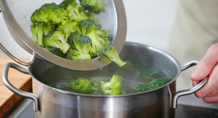 Frischer Brokkoli wird aus einem Sieb in einen Topf mit kochendem Wasser gegeben. Perfekt für eine gesunde Brokkoli-Pfanne.