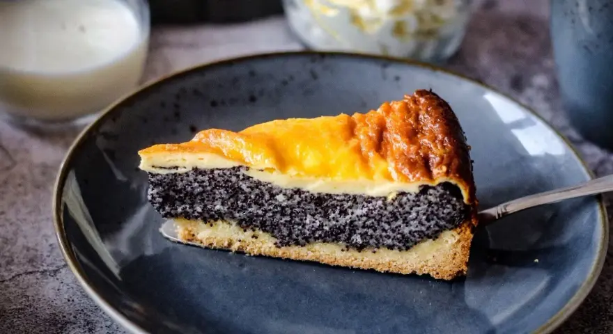 Ein saftiges Stück Mohnkuchen mit Pudding-Schicht auf einem blauen Teller, bereit zum Genuss.