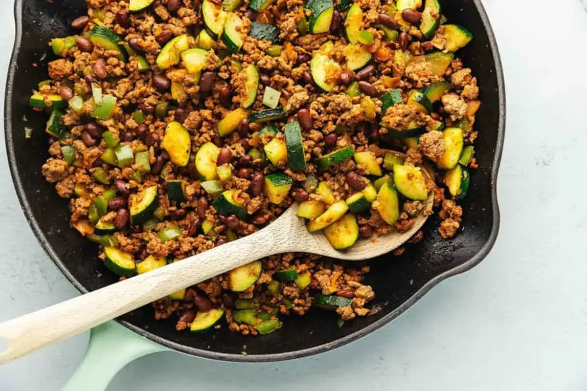 Herzhafte zucchini hackfleisch pfanne mit Bohnen und Paprika, serviert in einer Gusseisenpfanne mit einem Holzl&ouml;ffel.