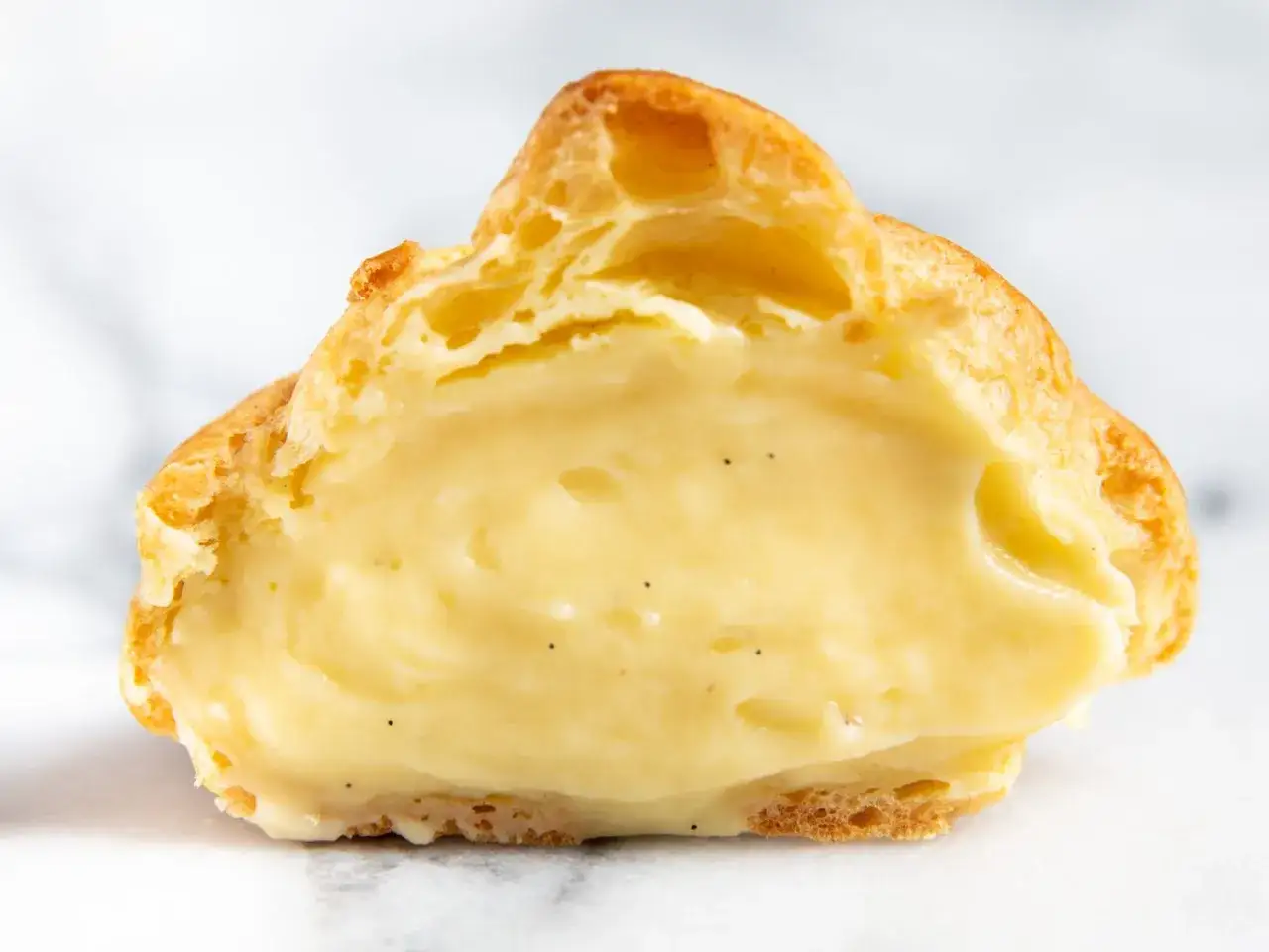 Ein aufgeschnittener Windbeutel, gefüllt mit cremiger Vanillecreme. Perfekt für ein Vanillecreme Rezept.