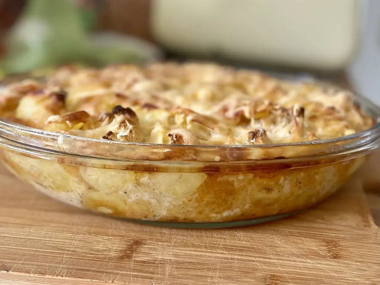 Ein goldbrauner Blumenkohlauflauf mit Kartoffeln und Käse in einer Glasschüssel, bereit zum Servieren.